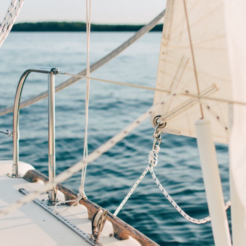 An view of the railing and rigging on a sailboat, with ocean waters in the background.